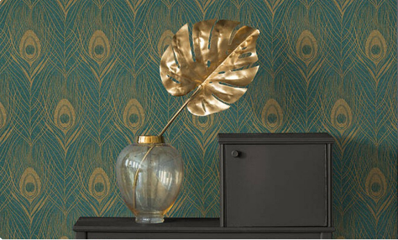 Decorative gold leaf in a clear vase against a peacock feather patterned wall.